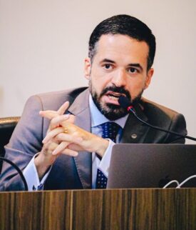 Thiago Mota, advogado criminalista e professor universitário de Maceió, em palestra técnica utilizando microfone e notebook.